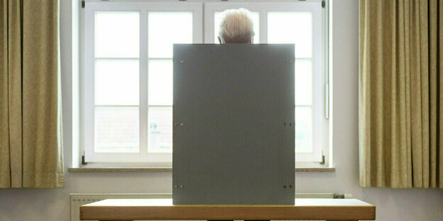 Windfried Kretschmann steht in einer Wahlkabine, zu sehen sind nur seine Haare