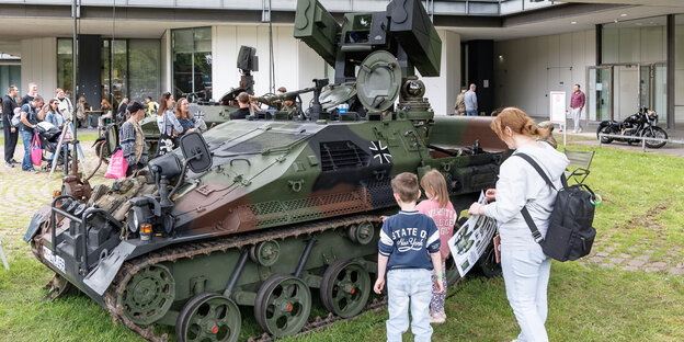Eine Mutter mit zwei Kinder steht vor einem Luftlandepanzer der Bundeswehr.