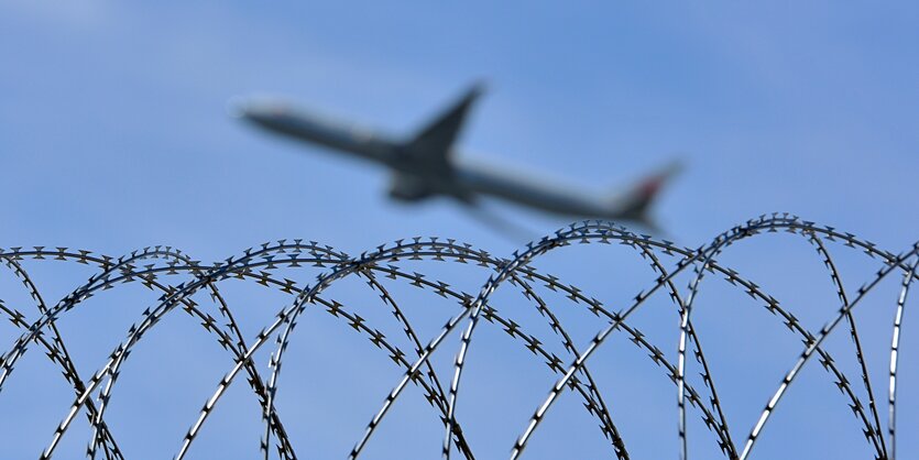 Ein Flugzeug fliegt über einen Stacheldrahtzaun. (Symbolbild)