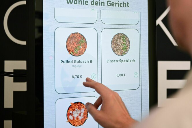 Eine Person wählt an einem Monitor ein Gericht aus