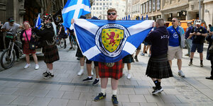 Schottische Fans halten auf dem münchner Marienplatz schottische Flaggen in die Höhe.