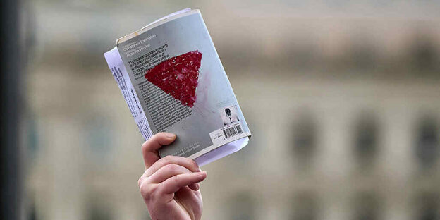 Eine Hand hält ein Buch, auf das ein rotes Dreieck gemalt ist