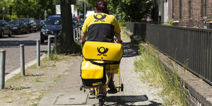 Eine Briefträgerin fährt mit ihrem Fahrrad auf einem Bürgersteig