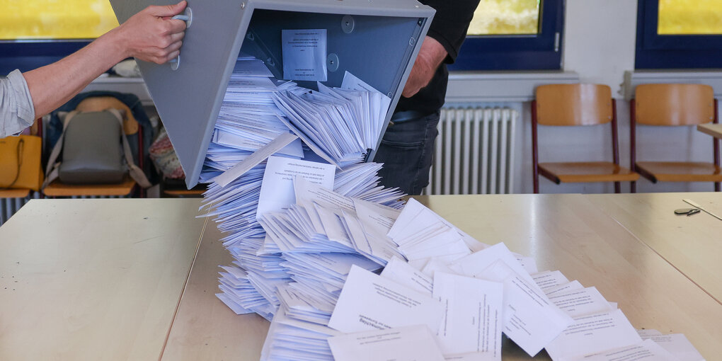 Wahlhelfer kippen eine Wahlurne nach der Europawahl zur Stimmenauszählung auf einen Tisch.