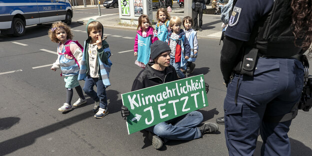 Ein Klima-Demonstrant sitzt auf der Straße während eine Gruppe von Kindern an ihm vorbei läuft.