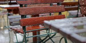 Regen tropft von den hölzernen Stühlen und Tischen eines Cafés.
