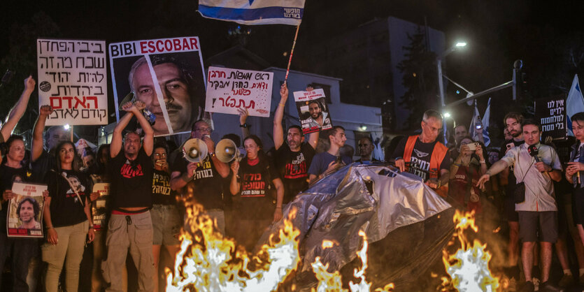 Menschen stehen in der Dunkelheit vor einem Feuer und halten Plakate in die Höhe