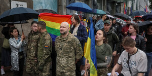 Soldaten und Soldateinnen demonstrieren gemeinsam mit menschen, die Regenbogenfahnen tragen