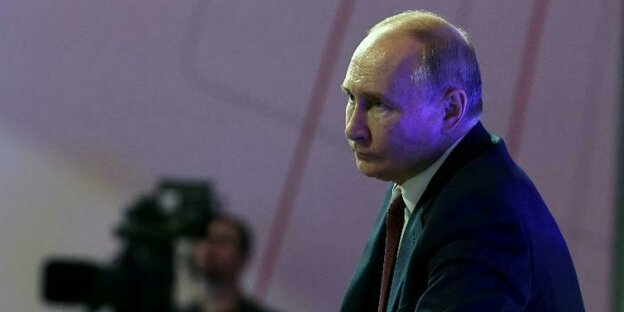 Wladimir Putin sitzt in einem Sessel mit einem Mikrofon in der Hand