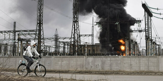 Ein Mann radelt an einem brennenden Elektrizitätswerk vorbei in Charkiw in der Ostukraine