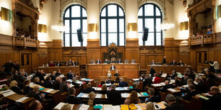 Menschen sitzen in einem Saal und gucken auf eine Rednerin vorn am Redepult