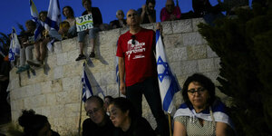 Menschen sitzen vor und auf einer Mauer bei einer Demo in Jerusalem