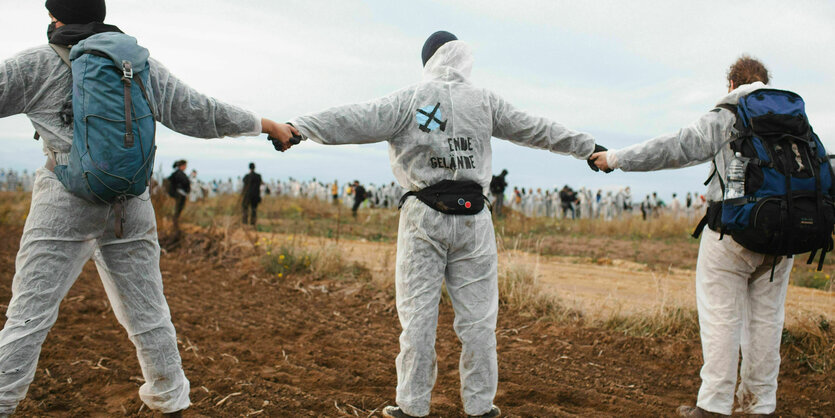 Aktivist:innen in weißen Anzügen auf einem Feld.