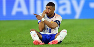 Der französische Fußball-Nationalspieler sitzt auf dem Rasen und hält sich an die blutende Nase