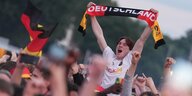 Ein Fußball-Fan im inoffiziellen Check24 Trikot hält einen Deutschland-Schal hoch