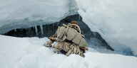 Mensch tief im Schnee vor einer Eishöhle