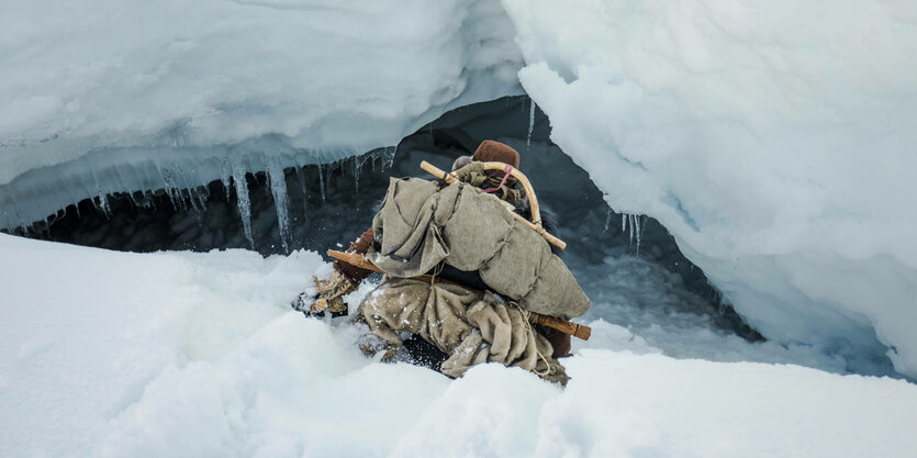 Mensch tief im Schnee vor einer Eishöhle