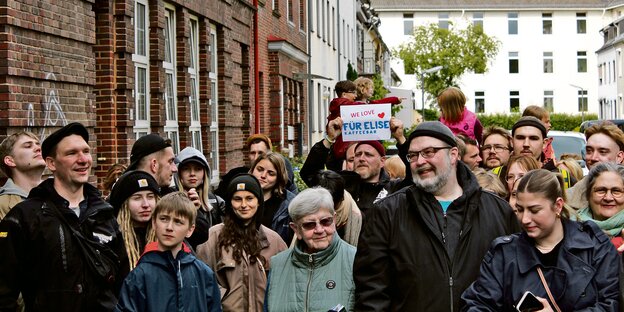 Eine Gruppe Menschen steht vor einer Häuserzeile. Ein Mann hält ein Schild mit der Aufschrift "We love Für Elise".