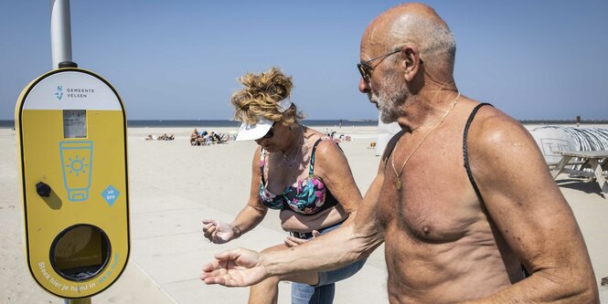 zwei Sonnenhungrige am Strand laufen auf einen Sonnencremespender zu