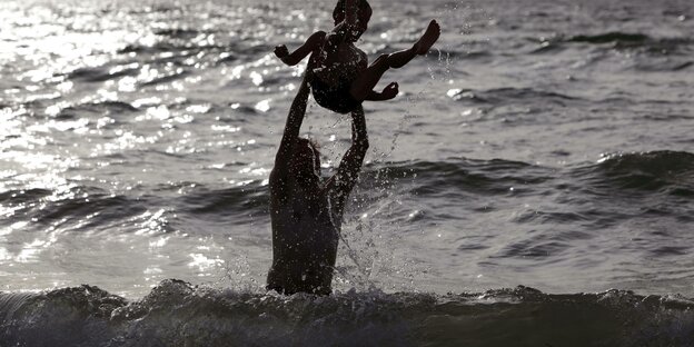 Ein Erwachsener und ein Kind toben an einem Strand.