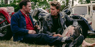 Danny (Tom Hardy, l.) und der im Gesicht leicht blutende Benny (Austin Butler) sitzen vor Motorrädern auf einer Wiese.