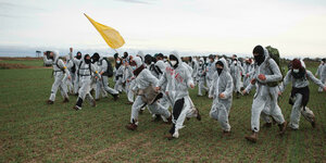 Aktivist:innen in weißen Anzügen rennen über ein Feld.