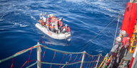 menschen stehen auf einem Rettungsschiff und blicken auf ein Beiboot