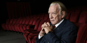 Donald Sutherland sitzt in einem leeren Kinosaal mit roten Samtsesseln, er trägt einen schwarzen Anzug und scheint in sich versunken