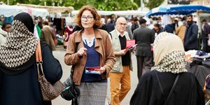 Agnès Cueille steht auf dem Markt von Dreux und verteilt Flyer an die Passanten, sie spricht mit zwei Frauen, die Kopftuch tragen