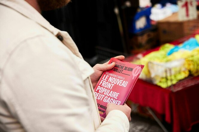 Eine Frau hält einen roter Flyer in der Hand, in der auf die "Front Populaire² hingewiesen wird