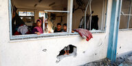 Eine Frau und zwei Jungen schauen aus einer Fensterhöhle in einer zerstörten Schule