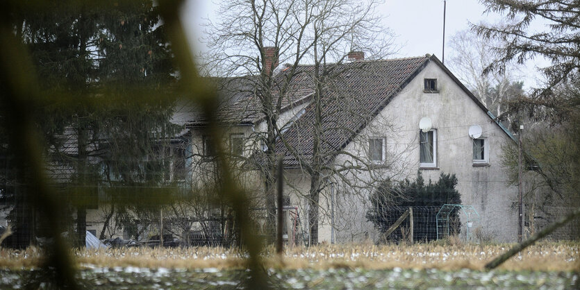 Ein unscheinbares Gebäude mit Satteldach hinter einem Zaun mit Satellitenschüsseln oberhalb von Fenstern