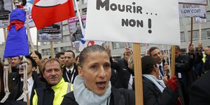 Bild von Demonstrierenden. Im Vordergrund eine Frau mit einem Plakat "Arbeiten oder Sterben.... Nein!"