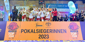Basketballerinnen jubeln auf einer Bühne, davor steht auf einem Schild: "Pokalsiegerinnen 2023"