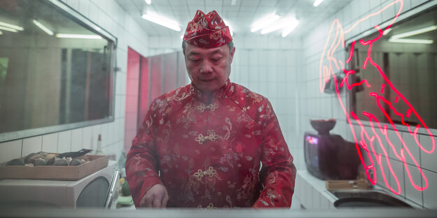 Ein Mann im chinesischen Gewand steht in einer Küche und schneidet etwas