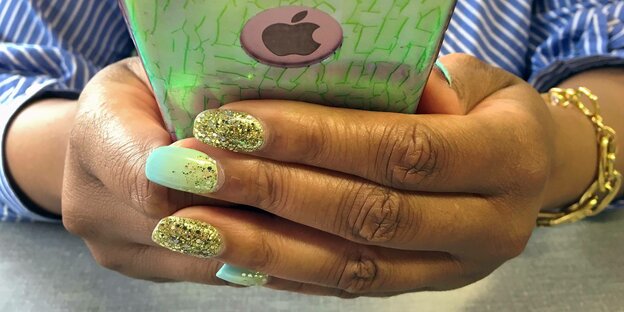 Eine Hand mit lackierten Nägeln mit Goldstaub hält ein Apple-Smartphone