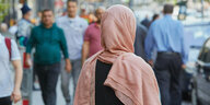 Eine Frau mit rosa Kopftuch von hinten auf einem Bürgersteig