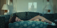 Die Protagonistin des Films liegt auf dem Sofa, in der Glasscheibe hinter ihr spiegelt sich eine männliche Figur