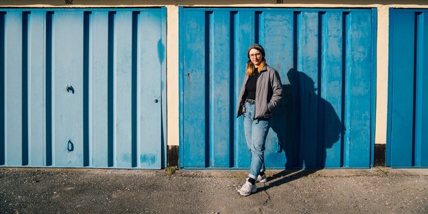 Alina Gündel steht in Jeans und Jacke vor blauen Garagentoren
