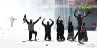 Junge Männer knien auf der ERde im Tränengasnebel und recken ihre Arme siegesgewiss in die Höhe