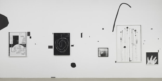 An einer Ausstellungswand hängen verschiedenen abstrakte Drucke in Schwarz-Weiß. Weitere geschwungene, abstrakte Formen wie Punkte und Striche sind direkt auf die Wand aufgetragen.