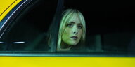 Die blonde Hauptdarstellerin blickt durch das getönte Fenster eines gelben Taxis