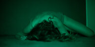 Frau liegt in grünem Licht leichtbekleidet auf dem Boden