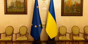 Eine ukrainische und eine europäische Flagge zwischen Ölgemälden und Stühlen