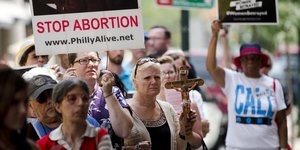 Menschen halten Schilder und ein Kreuz hoch, auf einem Schild steht: „Abtreibungen stoppen“