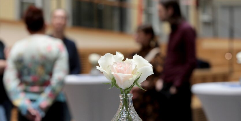 Im Vordergrund ein Sträusschen Rosen, im Hntergrund (unscharf) eine Gruppe von menschen