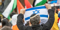 Ein Mann mit Kippa auf dem Kopf hält bei einer Demo eine Israel-Flagge hoch