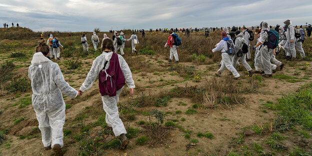 Menschen in weißen Schutzanzügen in einer steppigen Landschaft