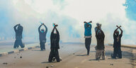 Menschen knien mit erhobenen Armen im Tränengasnebel