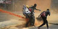 De­mons­tran­t*in­nen schützen sich vor den Wasserwerfern der Polizei in Nairobi